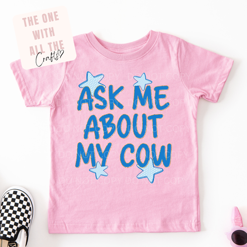 Pink t-shirt with blue text 'Ask Me About My Cow' on a white background