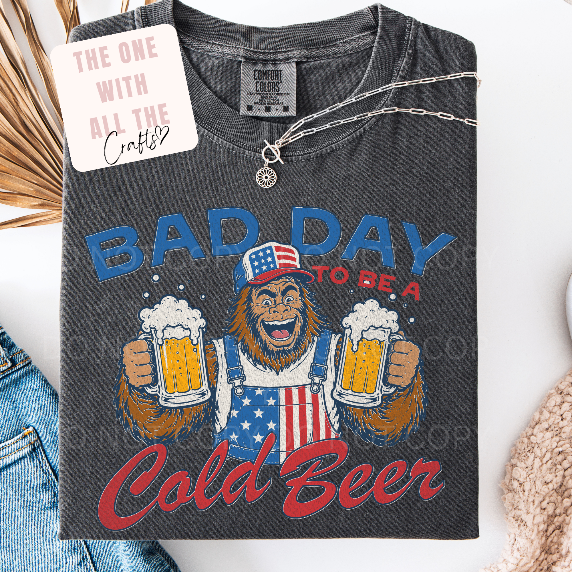 Gray t-shirt with a graphic of bigfoot holding beers and text 'Bad Day to be a Cold Beer' on a white background.