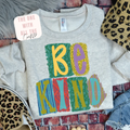 Gray sweatshirt with colorful 'BE KIND' text on a patterned surface