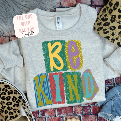 Gray sweatshirt with colorful 'BE KIND' text on a patterned surface