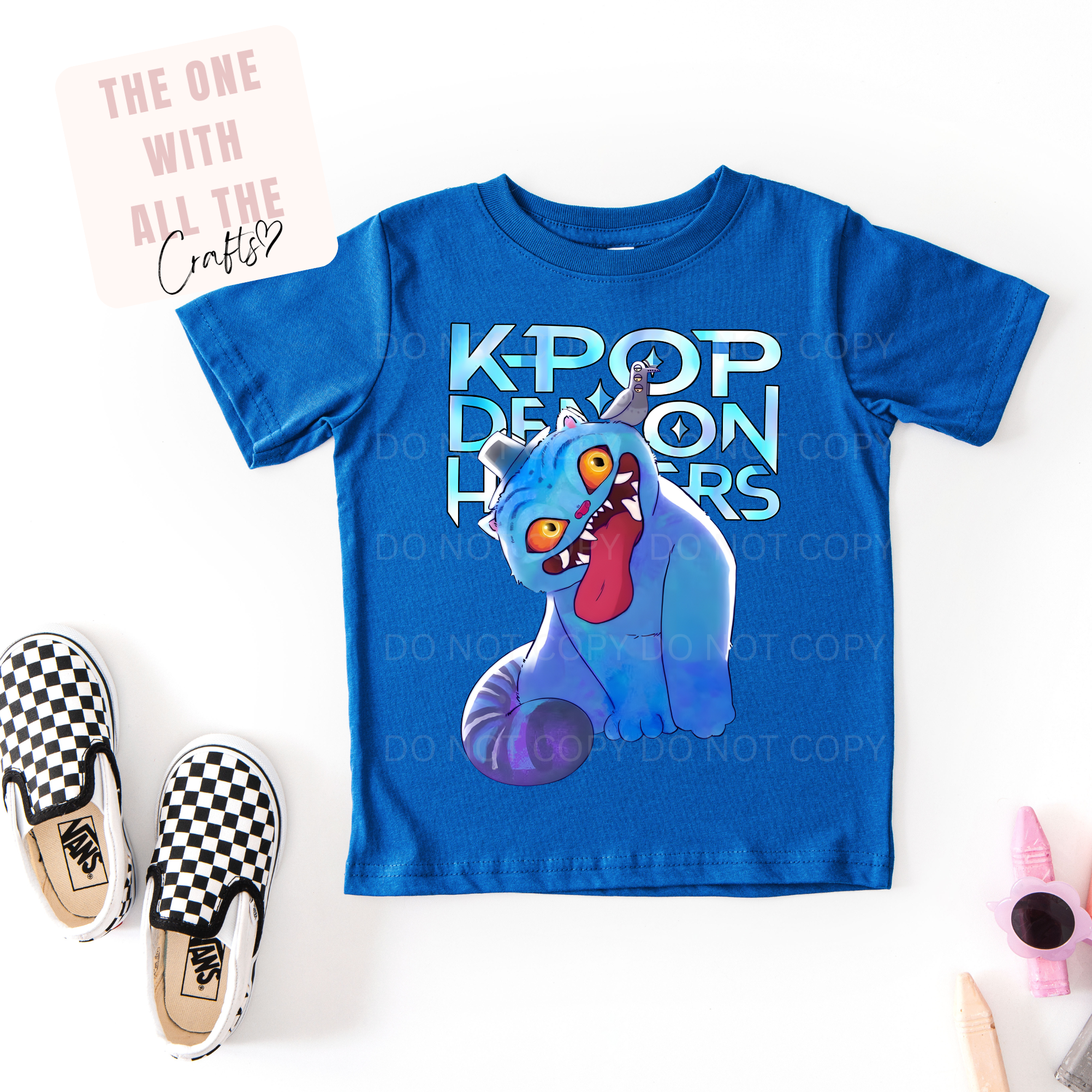Blue t-shirt with a blue creature graphic and 'K-Pop Demon Hunters' text, paired with checkered shoes on a white background.