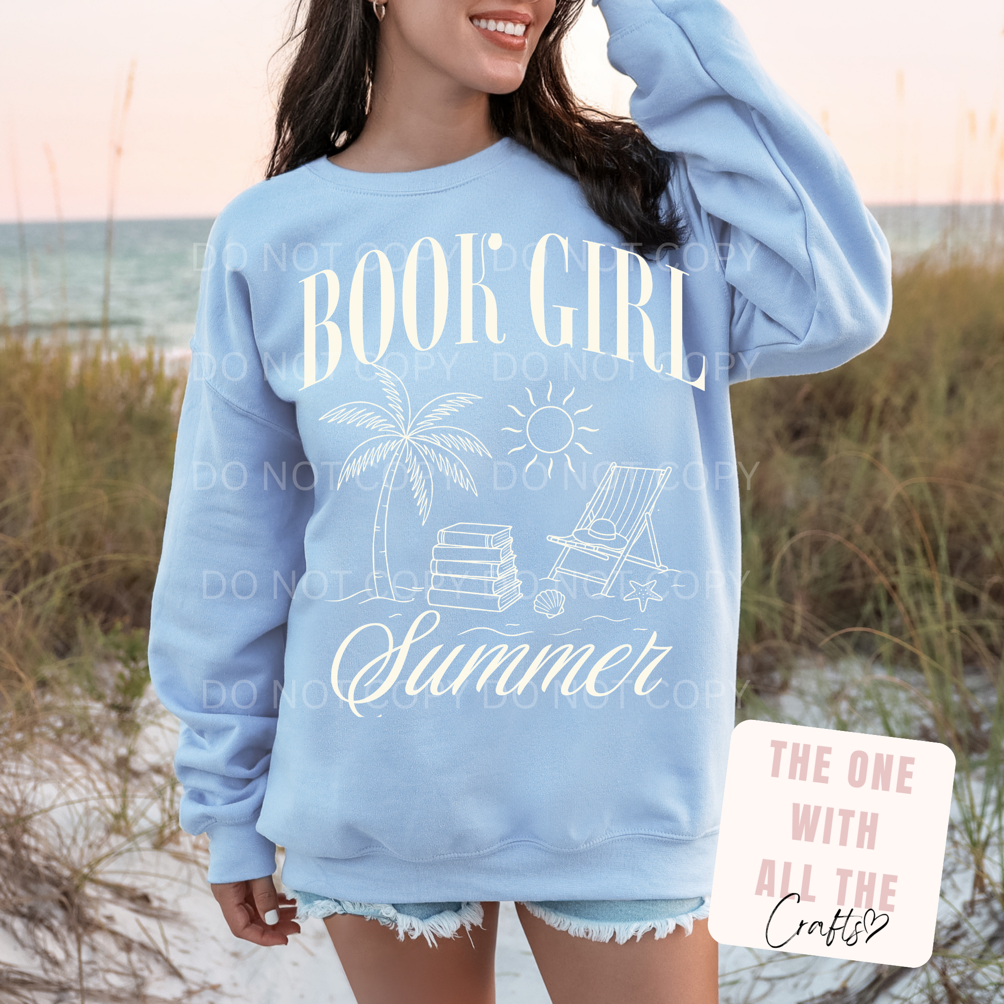 Person wearing a light blue sweatshirt with 'Book Girl Summer' text and beach graphics on a beach background.