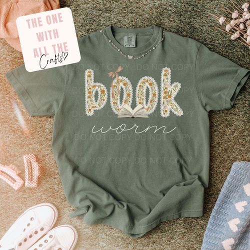 Green t-shirt with 'book worm' design on a textured surface with decorative items.