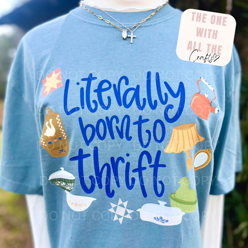 Blue t-shirt with 'Literally born to thrift' text and various graphics on a blurred background.