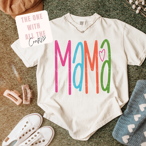 White t-shirt with 'Mama' in colorful letters on a textured surface with accessories.