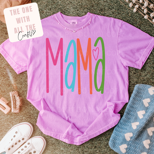 Pink t-shirt with 'MAMA' in colorful letters on a textured surface with accessories.