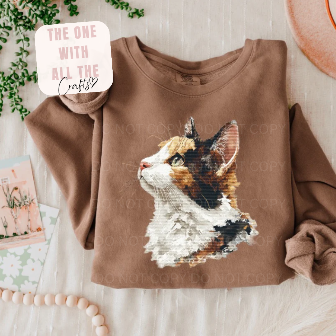 Brown sweatshirt with a cat graphic on a wooden surface