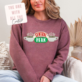 Person wearing a maroon sweatshirt with 'Central Perk' design, sitting on a couch.