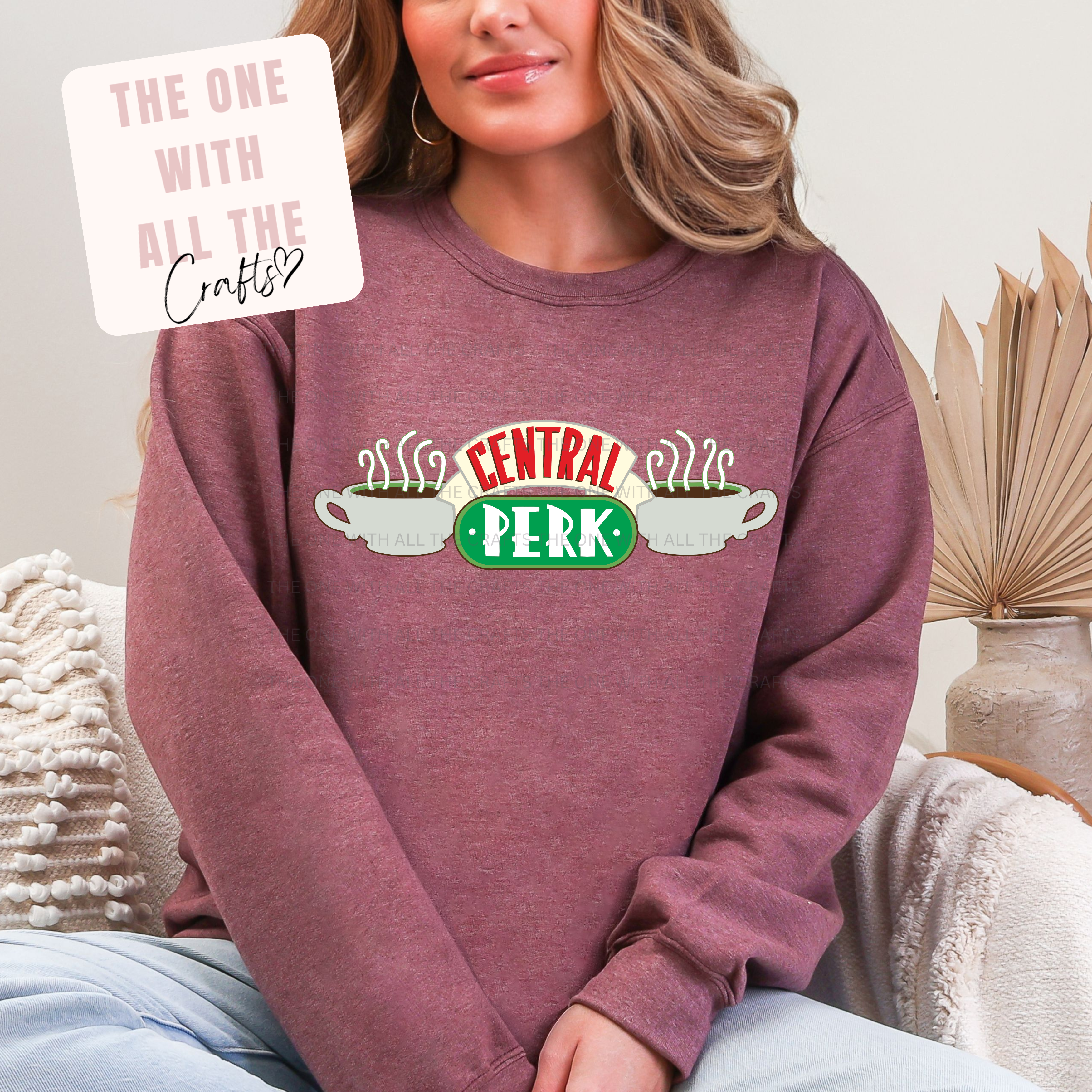 Person wearing a maroon sweatshirt with 'Central Perk' design, sitting on a couch.