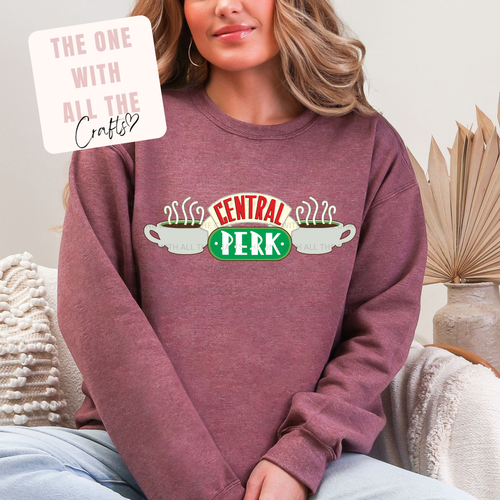 Person wearing a maroon sweatshirt with 'Central Perk' design, sitting on a couch.