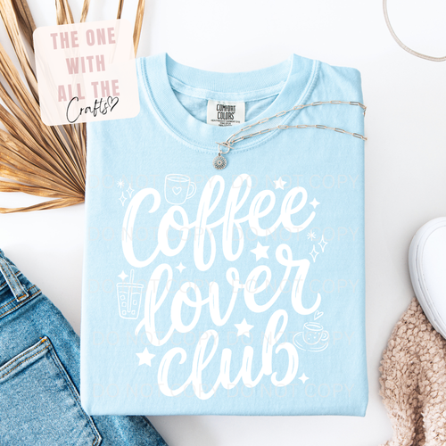 Light blue t-shirt with 'Coffee Lover Club' text on a white surface with accessories.