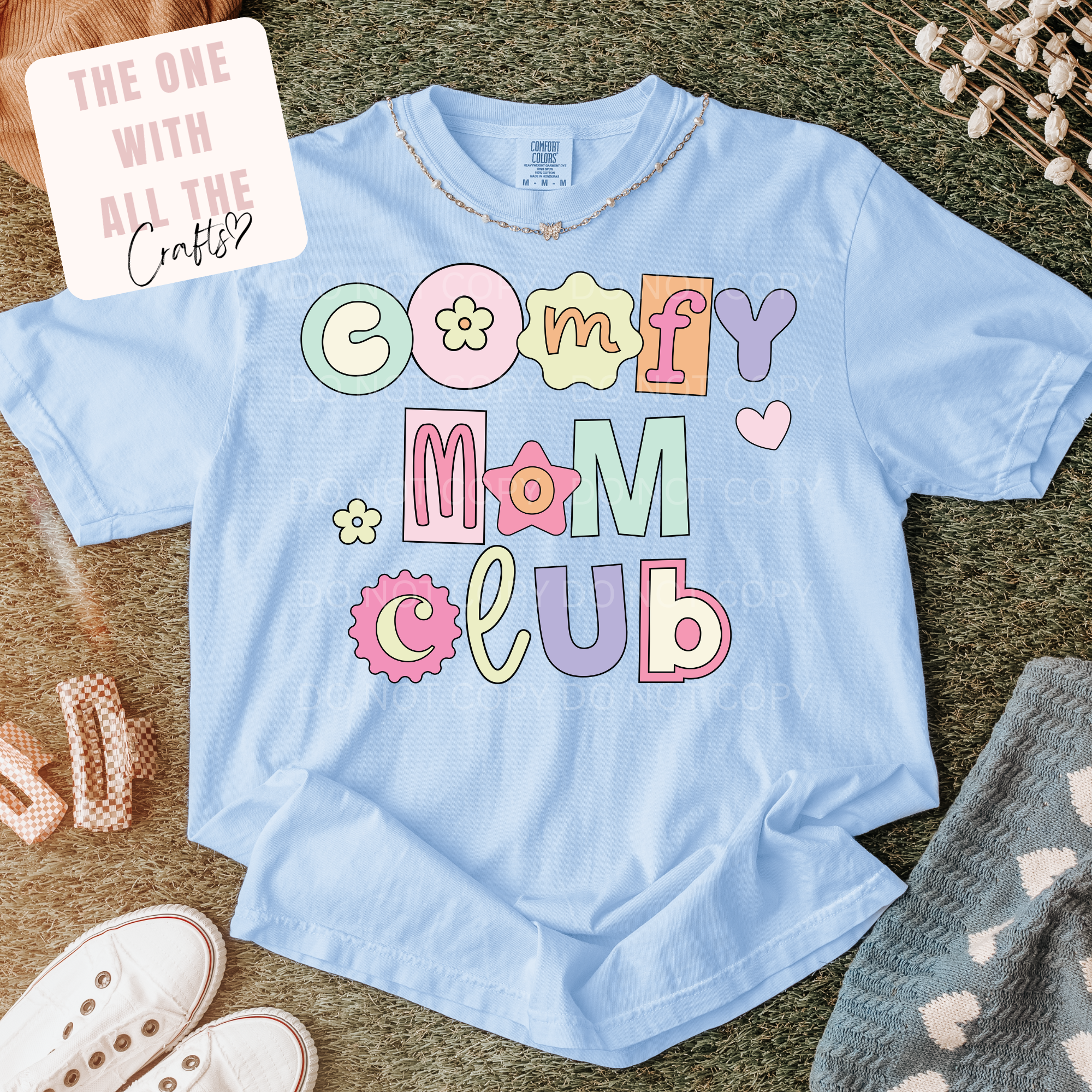 Light blue t-shirt with 'Comfy Mom Club' text on a textured surface with accessories.