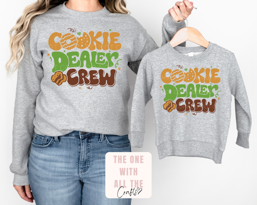 Gray sweatshirts with 'Cookie Dealer Crew' text, one worn by a person, the other on a hanger.