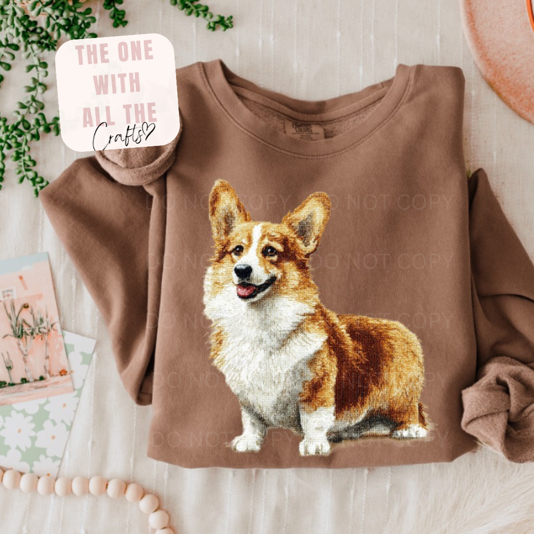 Brown sweatshirt with a corgi graphic on a light wooden surface.