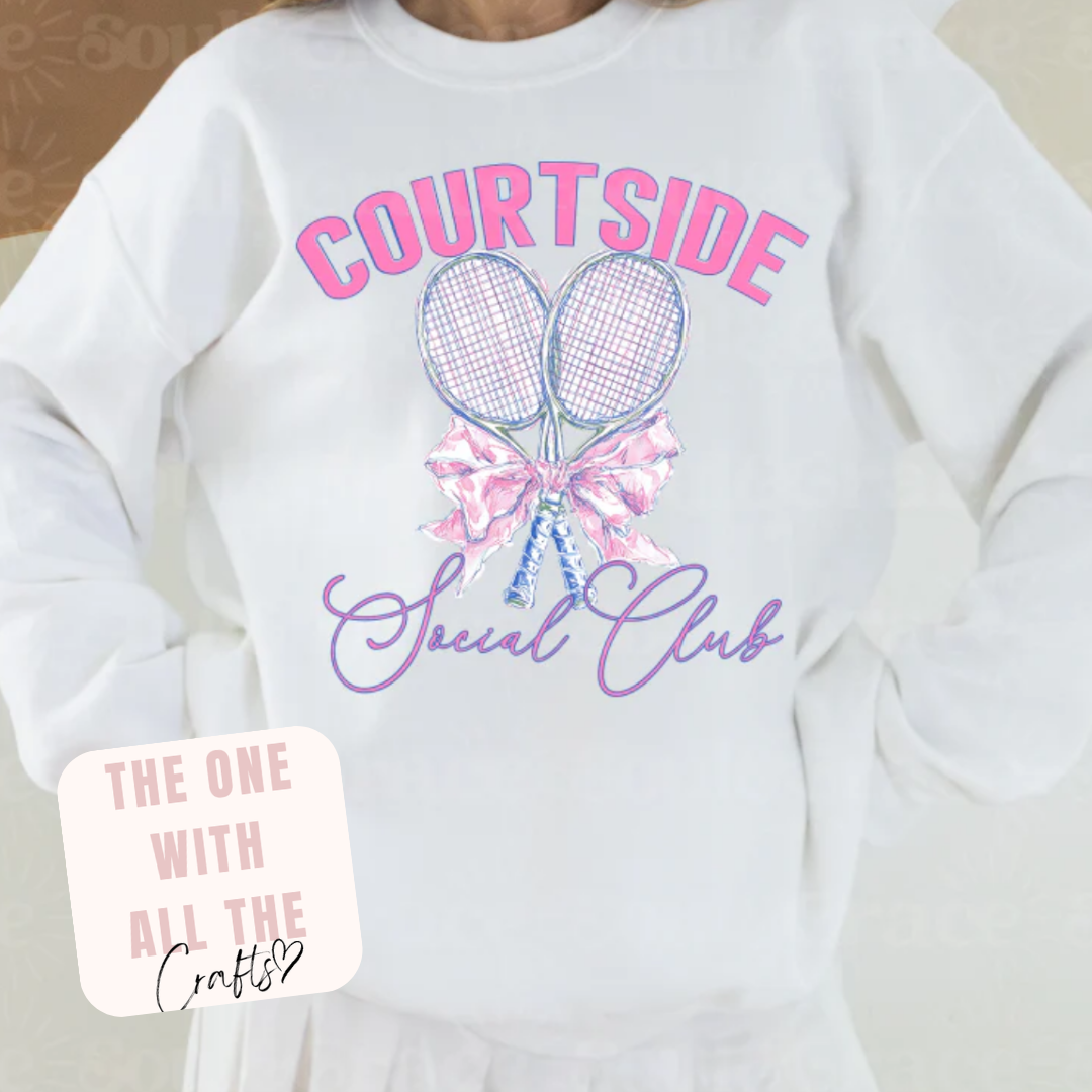 White sweatshirt with 'Courtside Social Club' design featuring tennis rackets and bows, worn by a person.