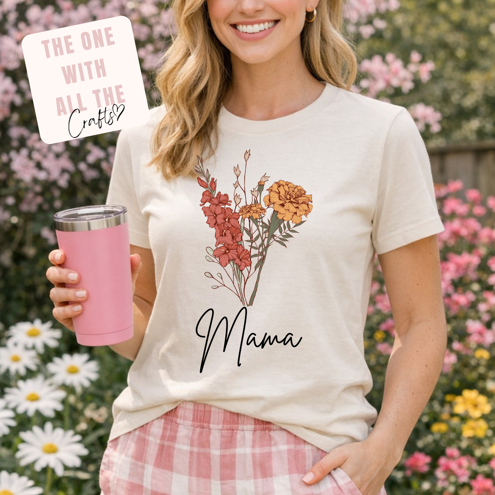 Woman wearing a white t-shirt with floral design and 'Mama' text, holding a pink cup in a garden setting.