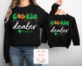 Black sweatshirts with 'Cookie Dealer' text and graphics on a plain background