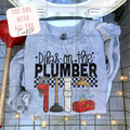 Gray shirt with plumbing-themed design and tools on a tiled bathroom floor.