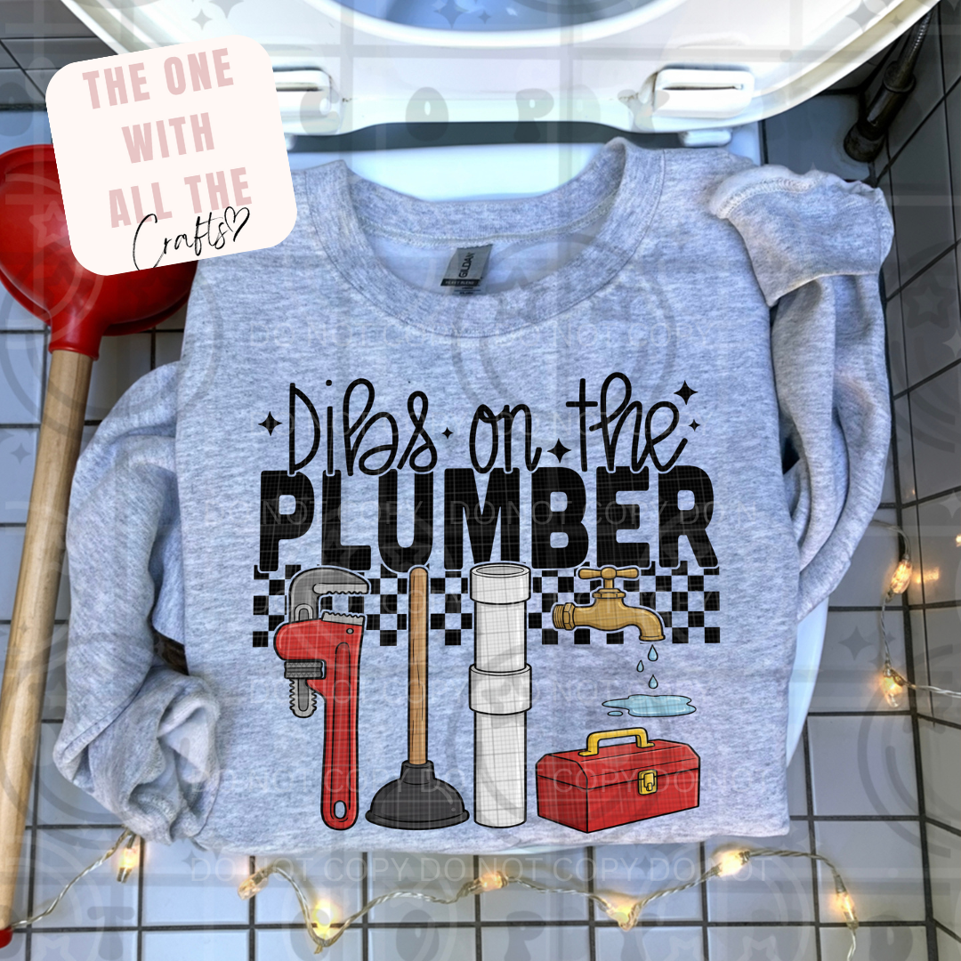 Gray shirt with plumbing-themed design and tools on a tiled bathroom floor.