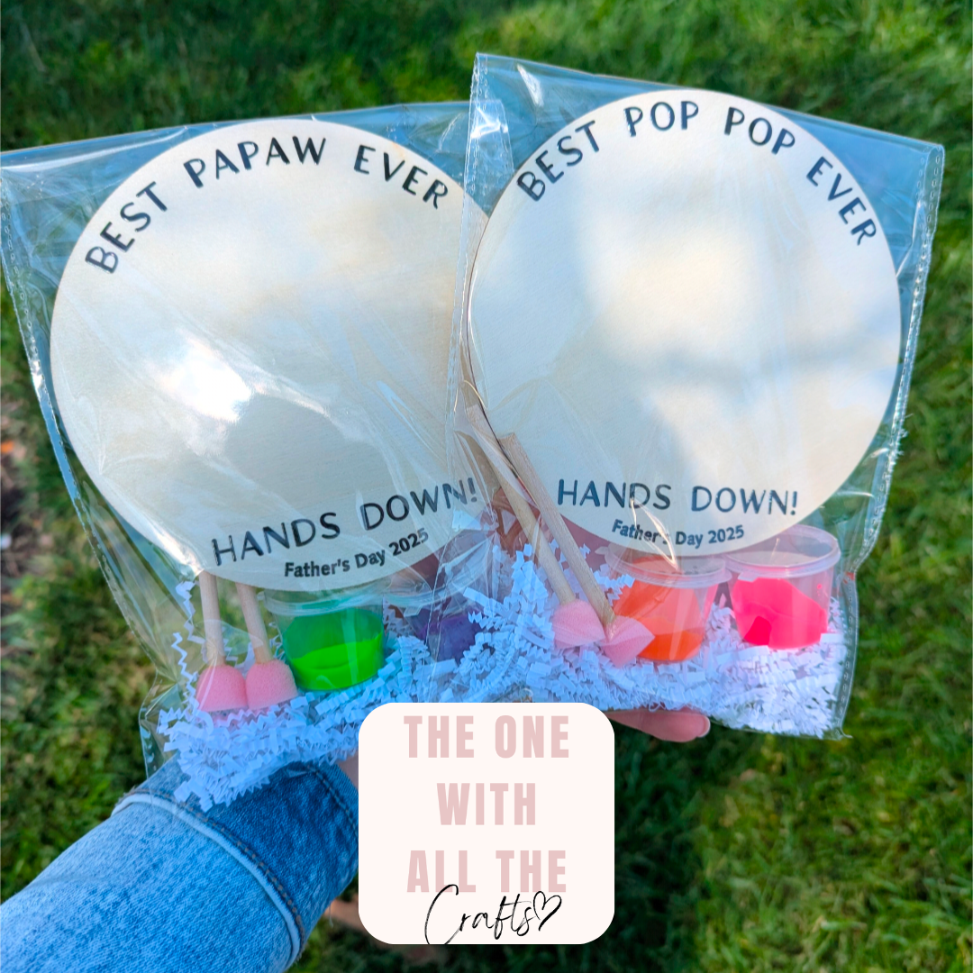 Two wooden craft circles with 'Best Papaw Ever Hands Down' text held in a clear package against a grass background.