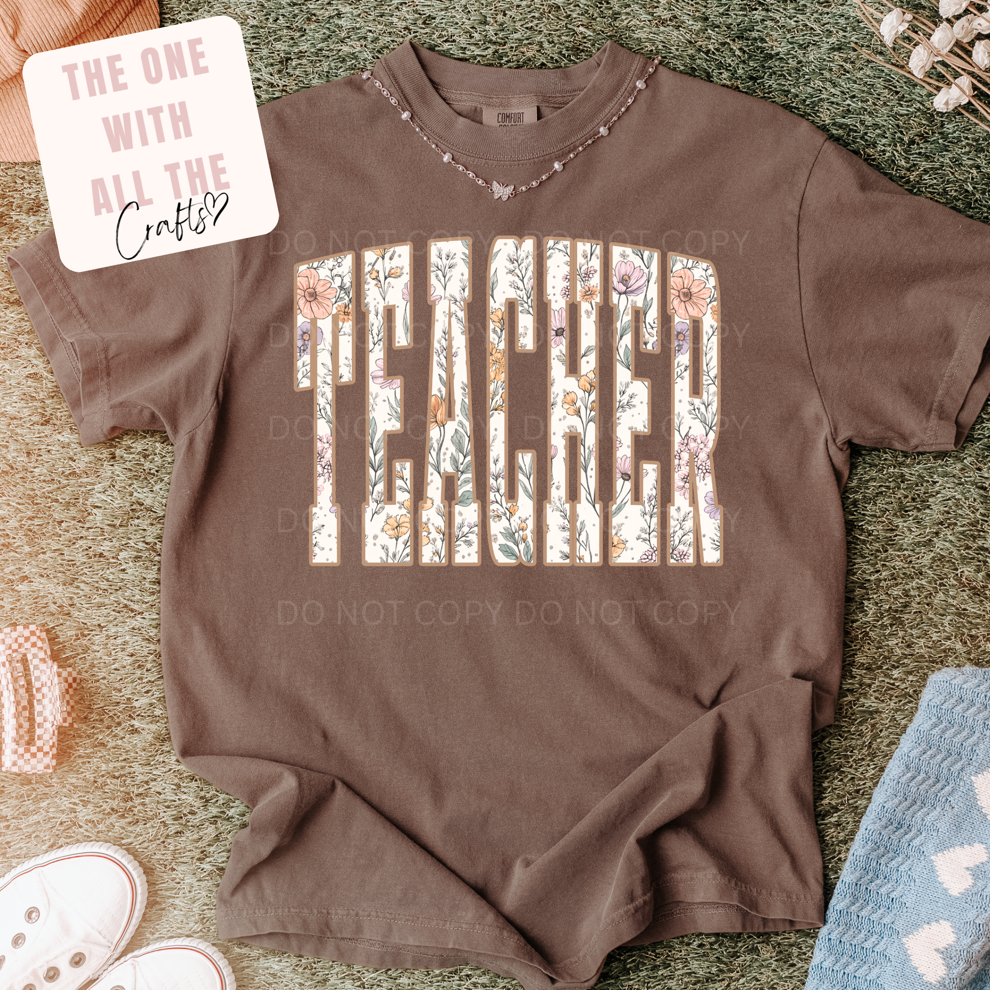 Brown t-shirt with 'Teacher' printed in floral letters on a textured surface.