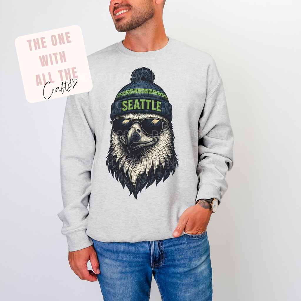 Person wearing a gray sweatshirt with a graphic of an eagle wearing sunglasses and a 'Seattle' beanie.