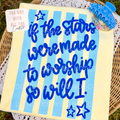 Decorative notebook with blue text and stars on a yellow background, placed on a woven surface.