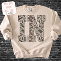 Beige sweatshirt with camouflage pattern letters 'IN' on a brick wall background