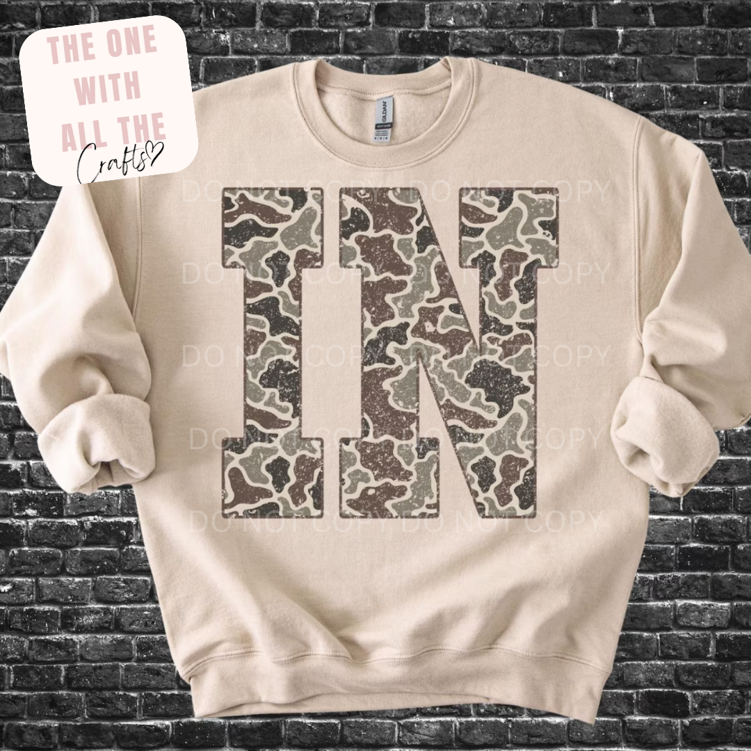 Beige sweatshirt with camouflage pattern letters 'IN' on a brick wall background