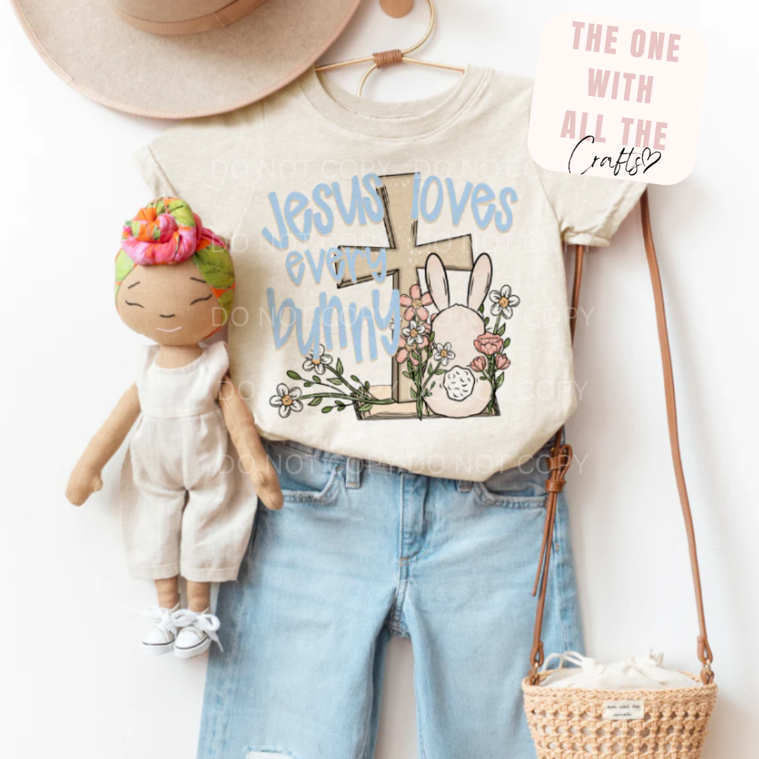 T-shirt with 'Jesus loves every bunny' design, doll, jeans, and straw bag on a white background