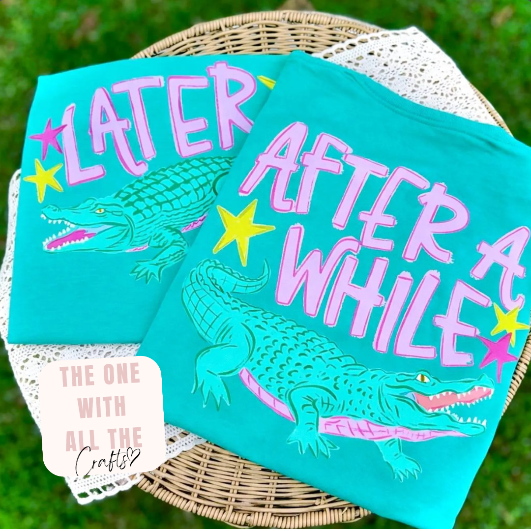 Two turquoise towels with alligator designs and text on a woven basket against a grassy background.