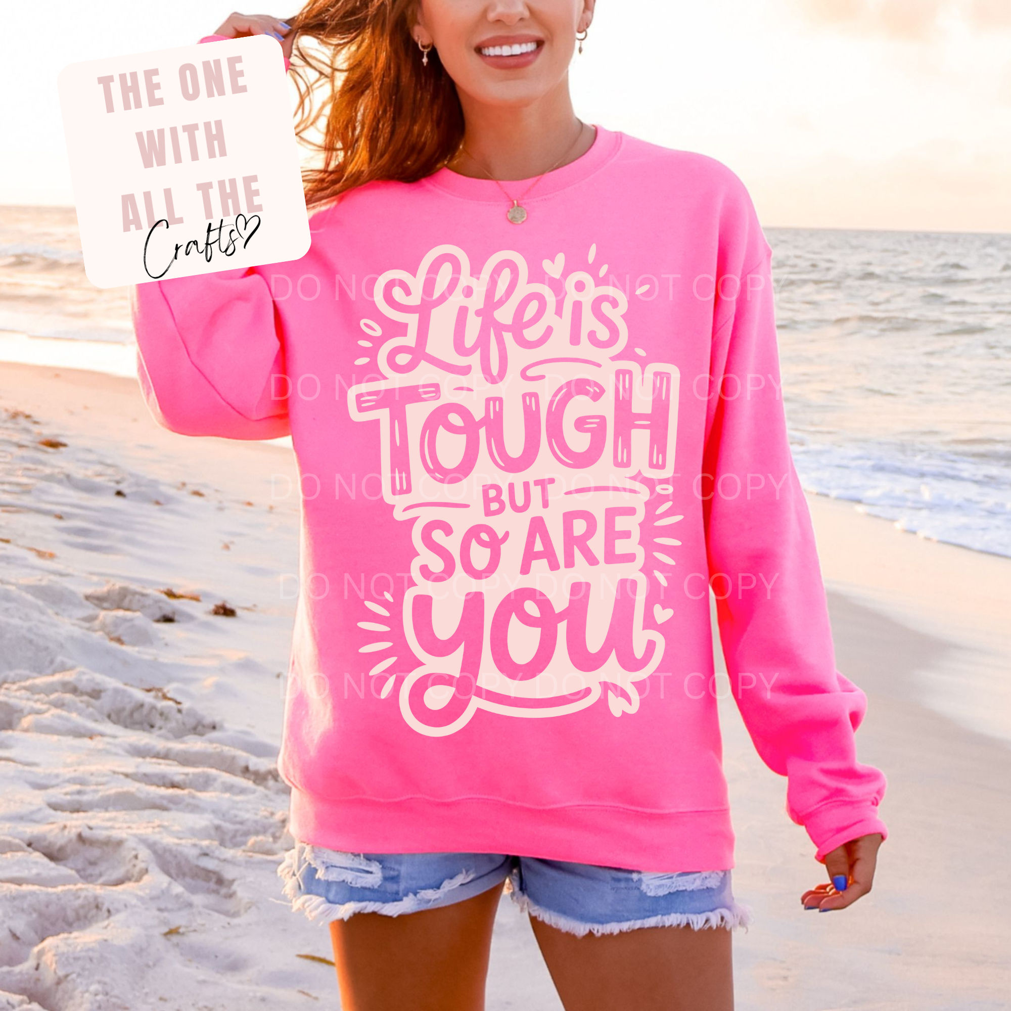 Person wearing a pink sweatshirt with 'Life is Tough but so are you' text on a beach.