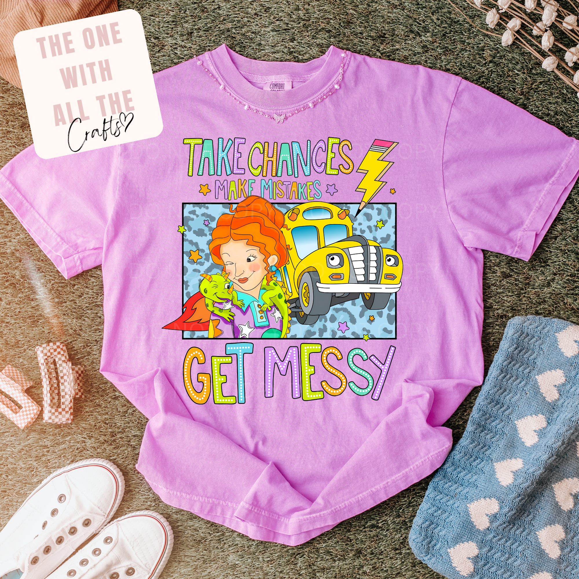 Purple t-shirt with colorful graphic and text on a textured surface with accessories. whimsy tee