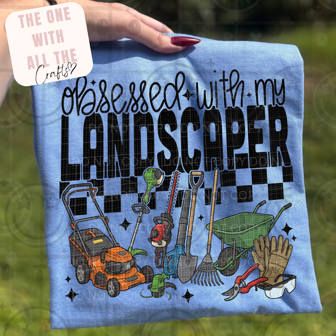 Shirt with gardening tools and text 'Obsessed with my landscaper' held by a hand.