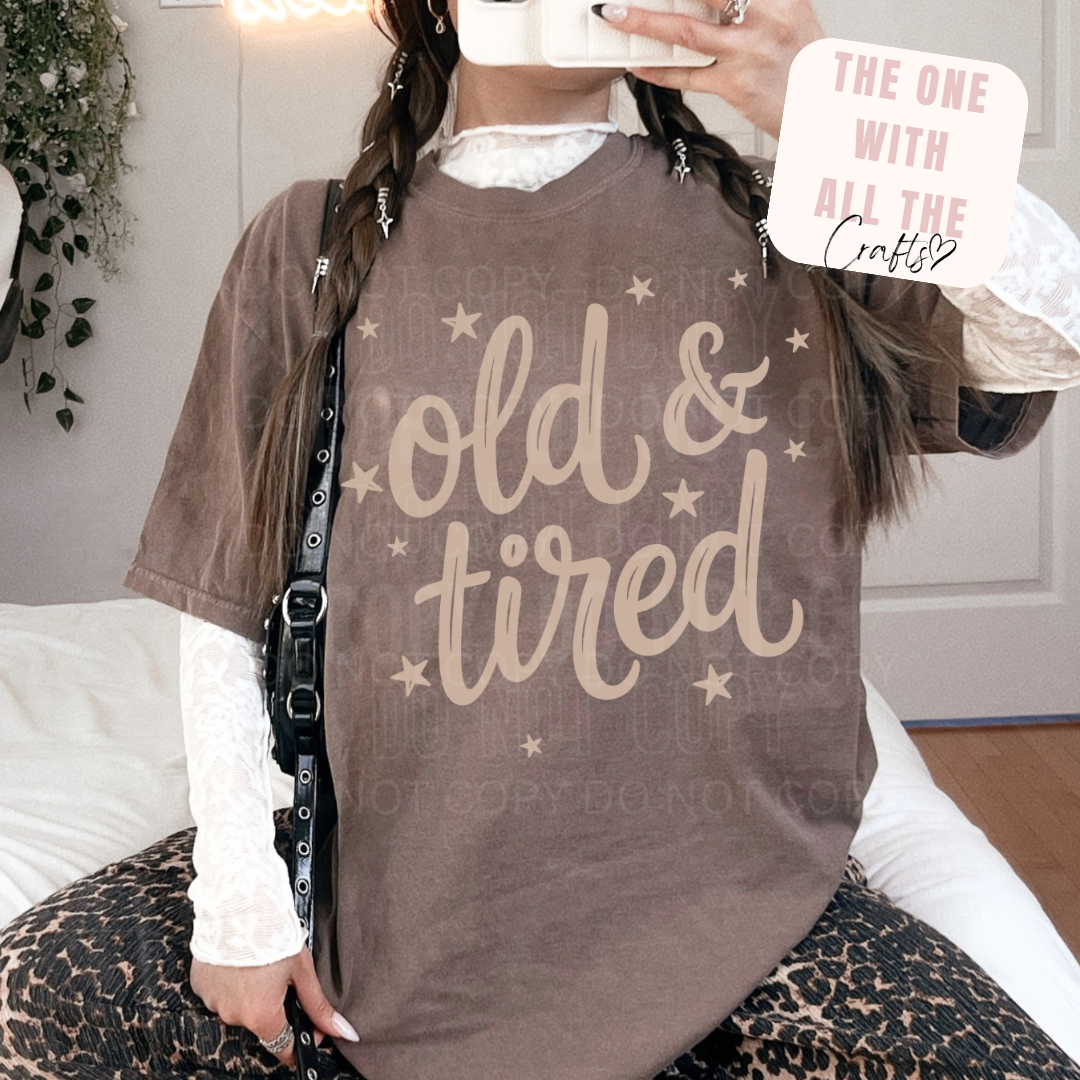 Person wearing a brown shirt with 'old & tired' text, holding a phone with text overlay.