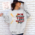 Person wearing a gray sweatshirt with a baseball design and text, standing against a white brick wall.