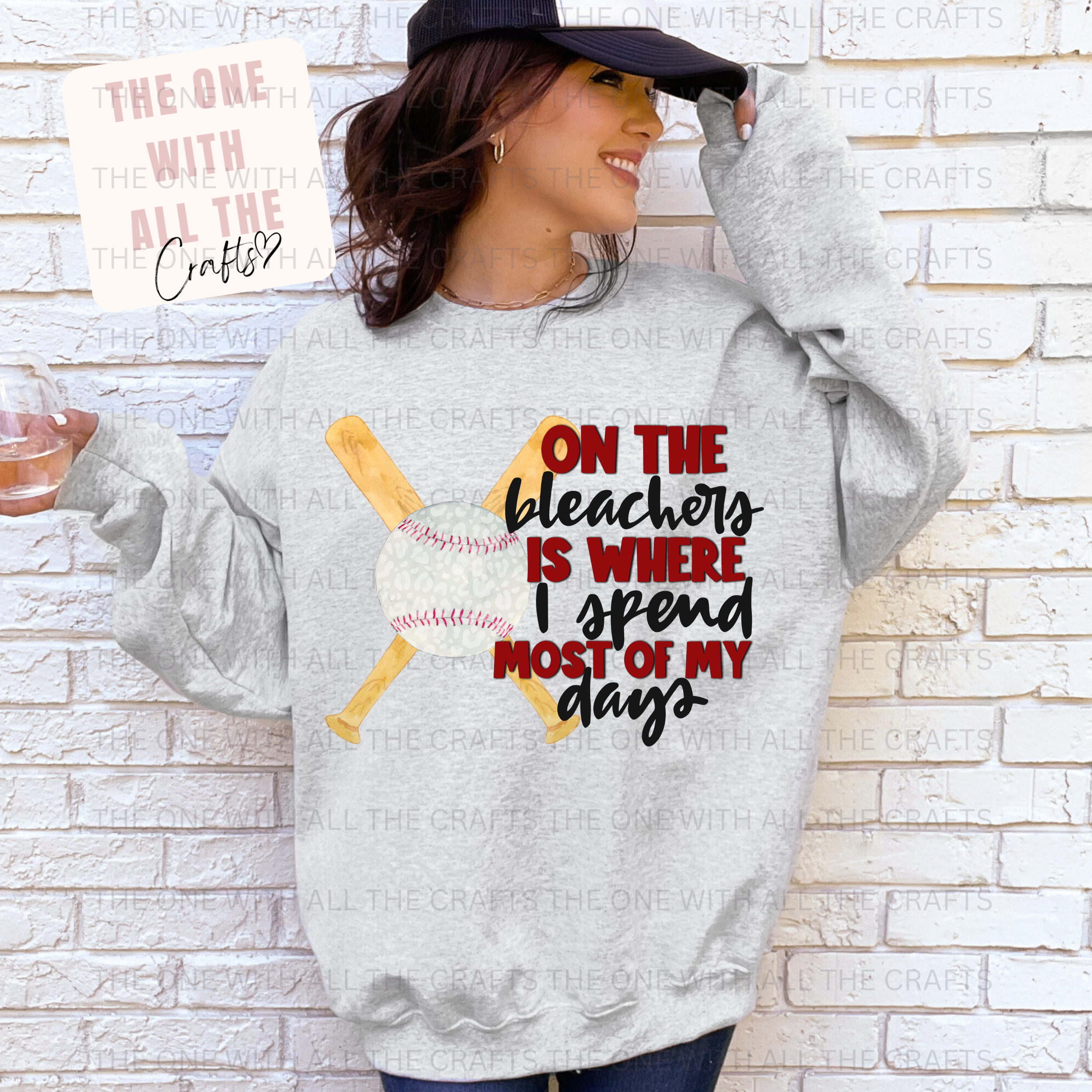Person wearing a gray sweatshirt with a baseball design and text, standing against a white brick wall.