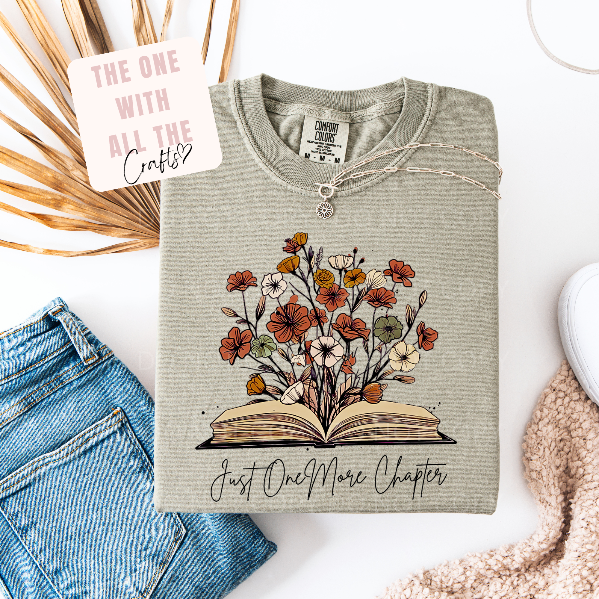 Folded sweatshirt with floral design and text on a white surface with denim jeans and decorative elements.