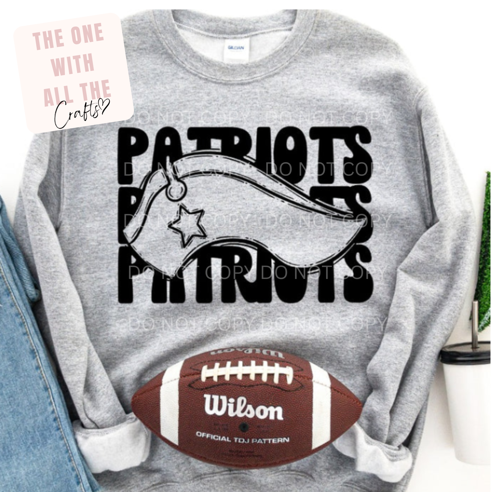 Gray sweatshirt with 'Patriots' text and football design, placed on a surface with a cup and card in the background.