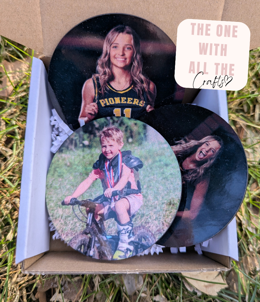 Three circular photo buttons with printed images of people, placed in a box on grass.