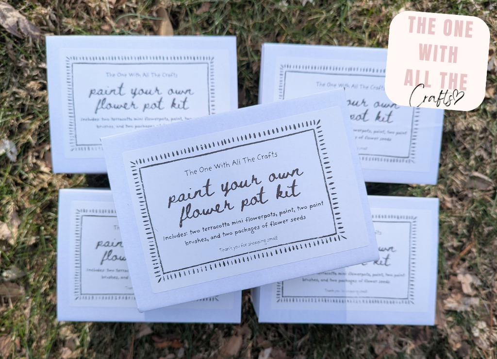 Packaging of 'Paint Your Own Flower Pot Kit' on grass. flower pot kit.