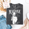 Black t-shirt with graphic design and text, paired with jeans and a necklace on a white surface.