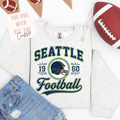 White t-shirt with 'Seattle Football' design, football and jeans on a white background