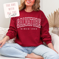 Person wearing a red sweatshirt with 'Salvatore Since 1864' text, sitting on a couch.