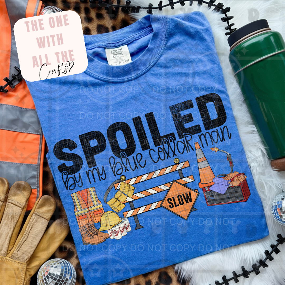 Blue t-shirt with 'Spoiled by my blue collar man' text and graphics, surrounded by construction-themed items.