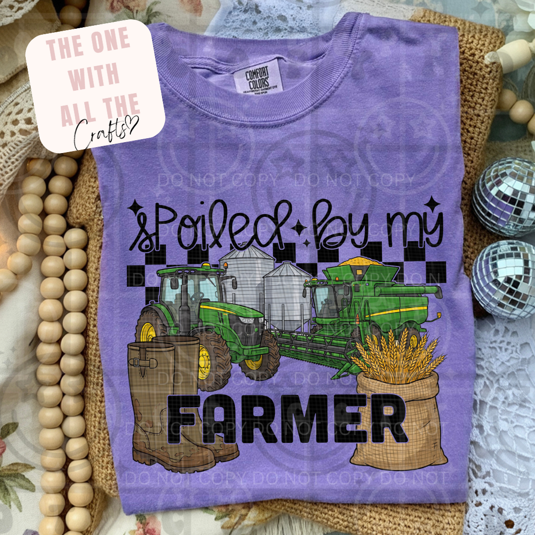 Purple t-shirt with farm-themed design featuring a tractor, boots, and grain sack on a textured surface.