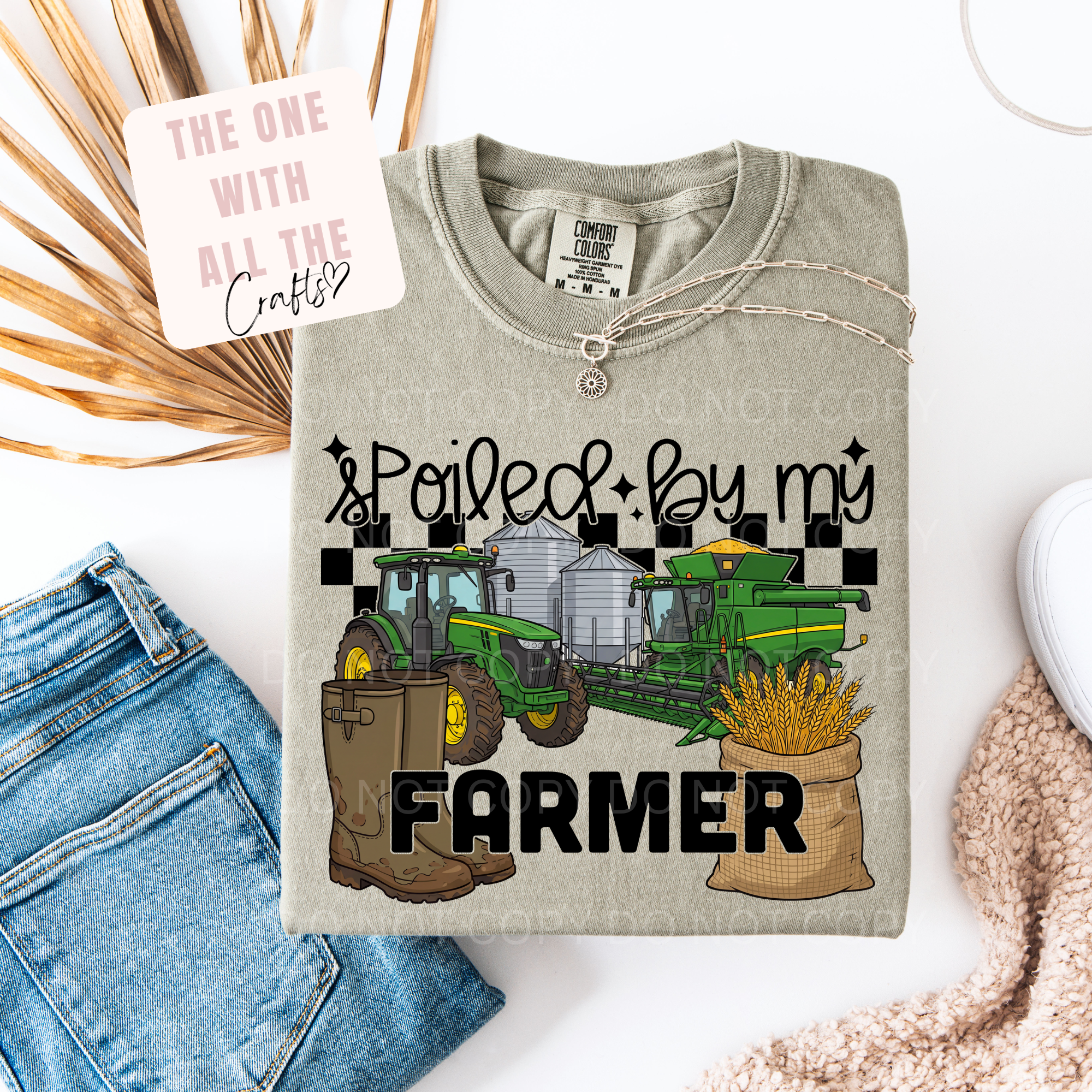 Gray t-shirt with farm-themed design and text 'Spoiled by my Farmer' on a white surface with denim jeans and decorative elements.