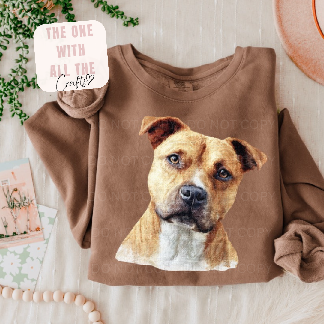 Brown sweatshirt with a dog's face printed on it, placed on a light surface with decorative items around.