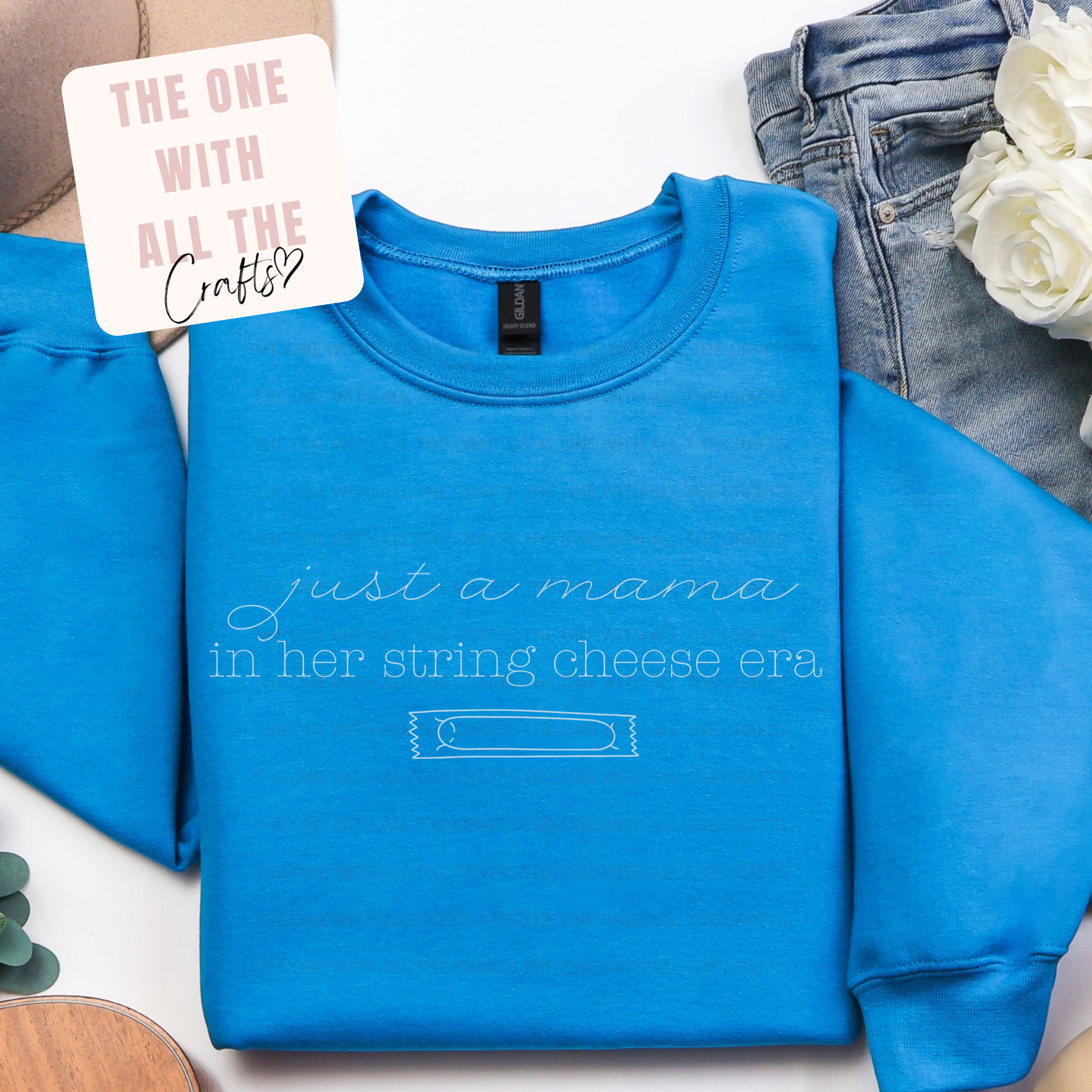 Blue sweatshirt with 'string cheese era' on a white surface with jeans and flowers. string cheese merch