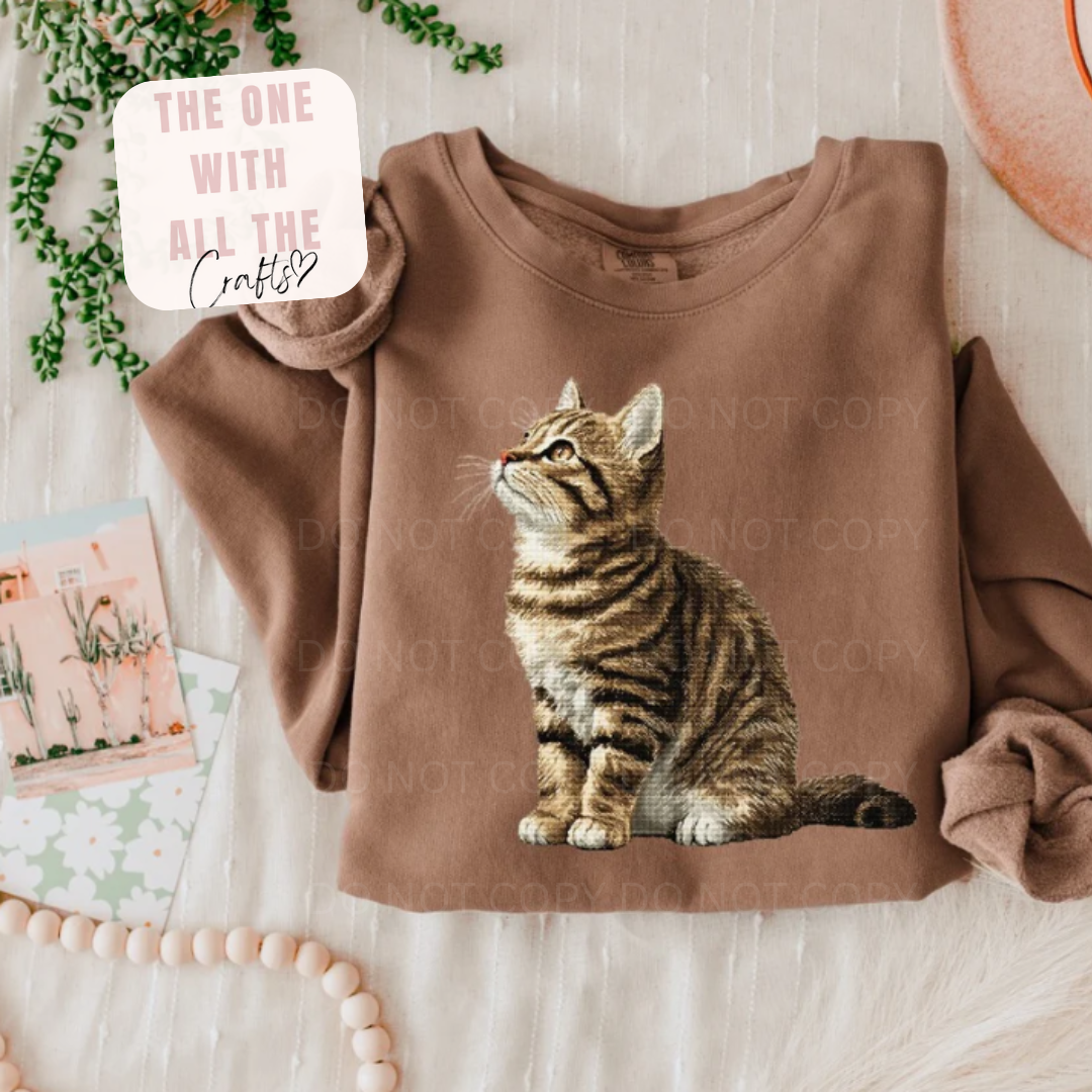 Brown sweatshirt with a cat graphic on a light wooden surface.